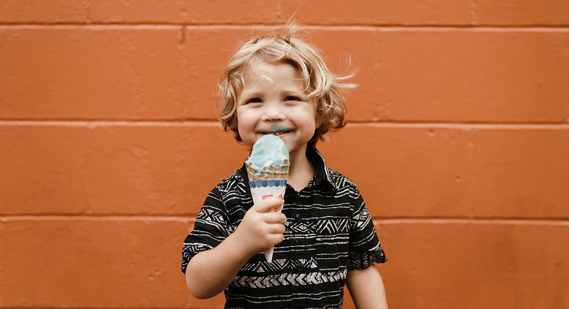 jeune garçon blond et souriant tenant un cornet de crème glacée