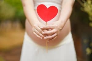 bédaine de femme enceinte tenant un bâton avec un coeur rouge en carton